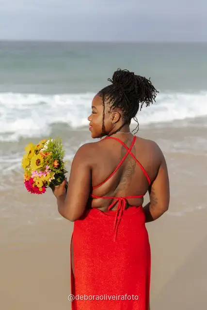 Woman in a long red dress holding a bouquet of sunflowers at the water line of Ipanema Beach in Rio de Janeiro