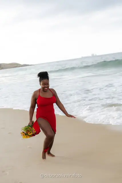 Woman in a red dress running and walking on Ipanema Beach with sunflowers under a cloudy sky