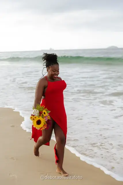 Woman in a red dress running and walking on Ipanema Beach with sunflowers under a cloudy sky
