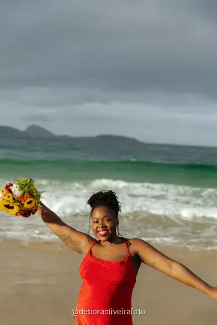 Woman in a red dress running and walking on Ipanema Beach with sunflowers under a cloudy sky