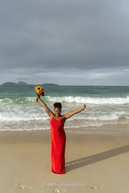 Woman in a red dress running and walking on Ipanema Beach with sunflowers under a cloudy sky
