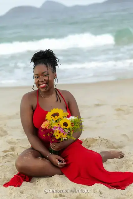Woman in a red dress sitting on the sand of Ipanema Beach with a sunflower bouquet