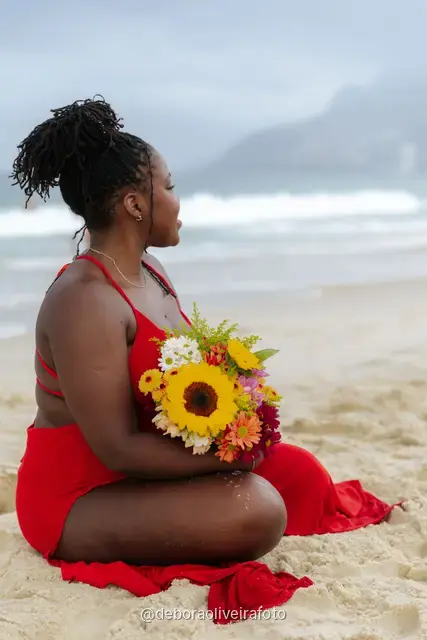 Woman in a red dress sitting on the sand of Ipanema Beach with a sunflower bouquet