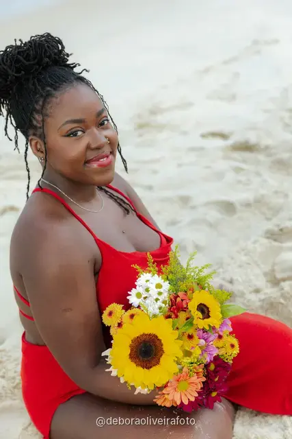Woman in a red dress sitting on the sand of Ipanema Beach with a sunflower bouquet