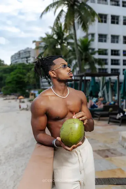Shirtless man holding a green coconut on a beachfront deck in Rio de Janeiro