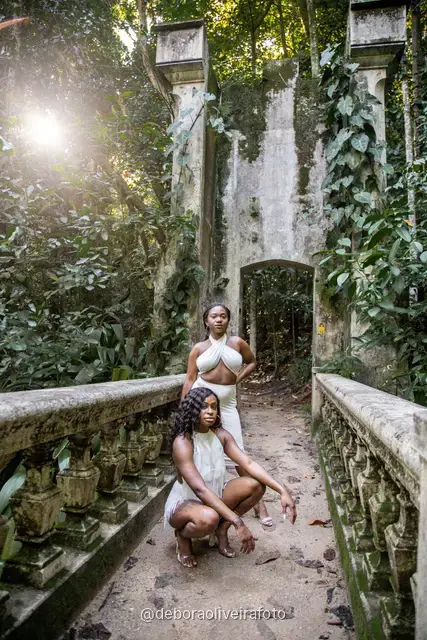 Two women in white sitting on the old bridge and on a fallen log at Parque Lage in Rio de Janeiro