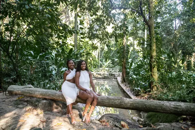 Two women in white sitting on the old bridge and on a fallen log at Parque Lage in Rio de Janeiro