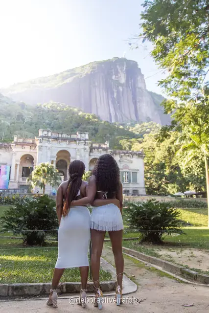 Two women in white in the garden in front of the Parque Lage mansion with the mountain behind