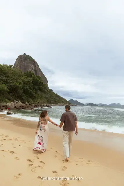 Pareja caminando y bailando en la orilla de Praia Vermelha con el Pan de Azúcar detrás
