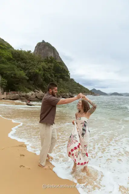 Pareja caminando y bailando en la orilla de Praia Vermelha con el Pan de Azúcar detrás