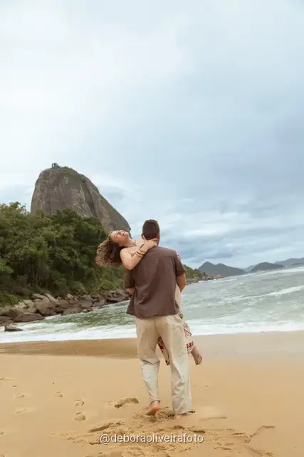 Hombre levantando a una mujer en la arena de Praia Vermelha con el Pan de Azúcar detrás