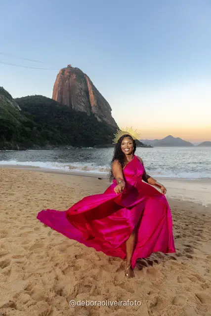 Woman in a pink flying dress at Praia Vermelha at sunset with Sugarloaf Mountain behind