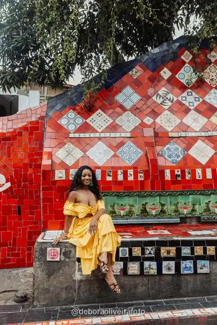 Woman in a yellow ruffled outfit at the red tile walls and ribbons of the Selarón Steps in Santa Teresa