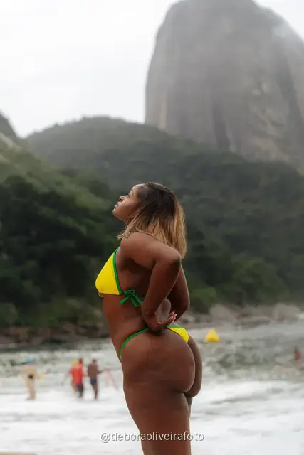 Mujer de amarillo y verde en Praia Vermelha con el Pan de Azúcar detrás, en Río de Janeiro