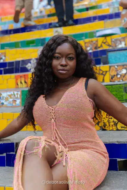 Woman in a long peach crochet dress sitting on the colorful tiled Selarón Steps in Rio de Janeiro