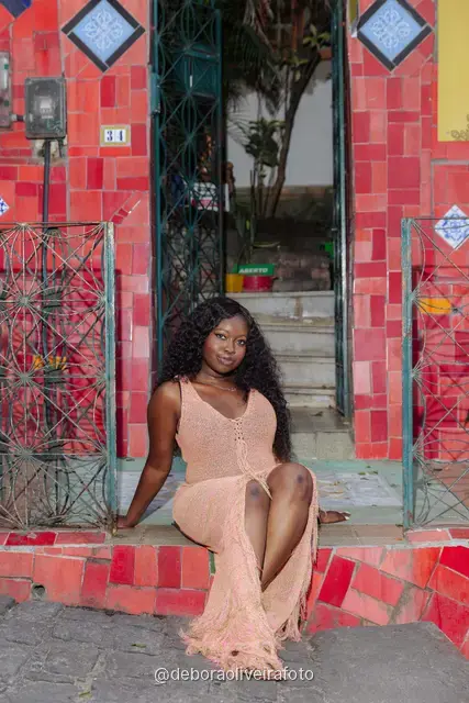 Mujer con vestido de crochet durazno frente a la pared de azulejos rojos y el mural amarillo de la Escalinata Selarón