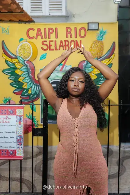 Mujer con vestido de crochet durazno frente a la pared de azulejos rojos y el mural amarillo de la Escalinata Selarón