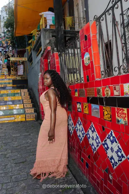 Mujer con vestido durazno apoyada en una pared de azulejos rojos en la callejuela junto a la Escalinata Selarón, en Santa Teresa