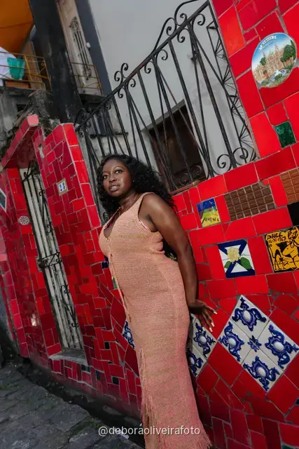 Mujer con vestido durazno apoyada en una pared de azulejos rojos en la callejuela junto a la Escalinata Selarón, en Santa Teresa