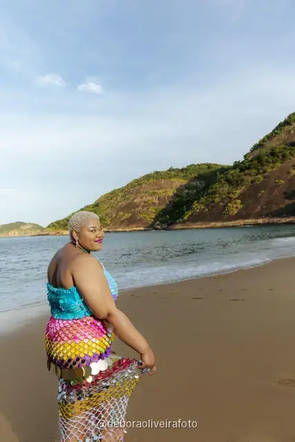Woman in a sequin mermaid look walking in the water at Praia Vermelha with Sugarloaf Mountain behind