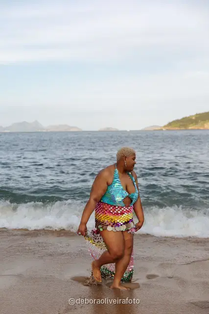 Woman in a sequin mermaid look walking in the water at Praia Vermelha with Sugarloaf Mountain behind